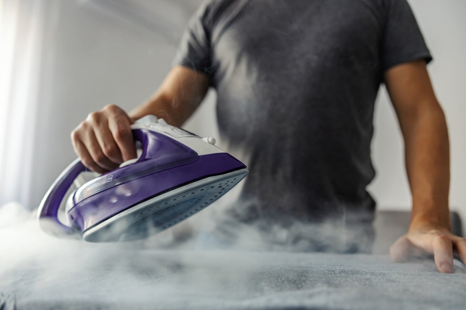 Powerful professional photo effect of water vapor from the hot iron. A modern lifestyle concept, a man who irons clothes at home