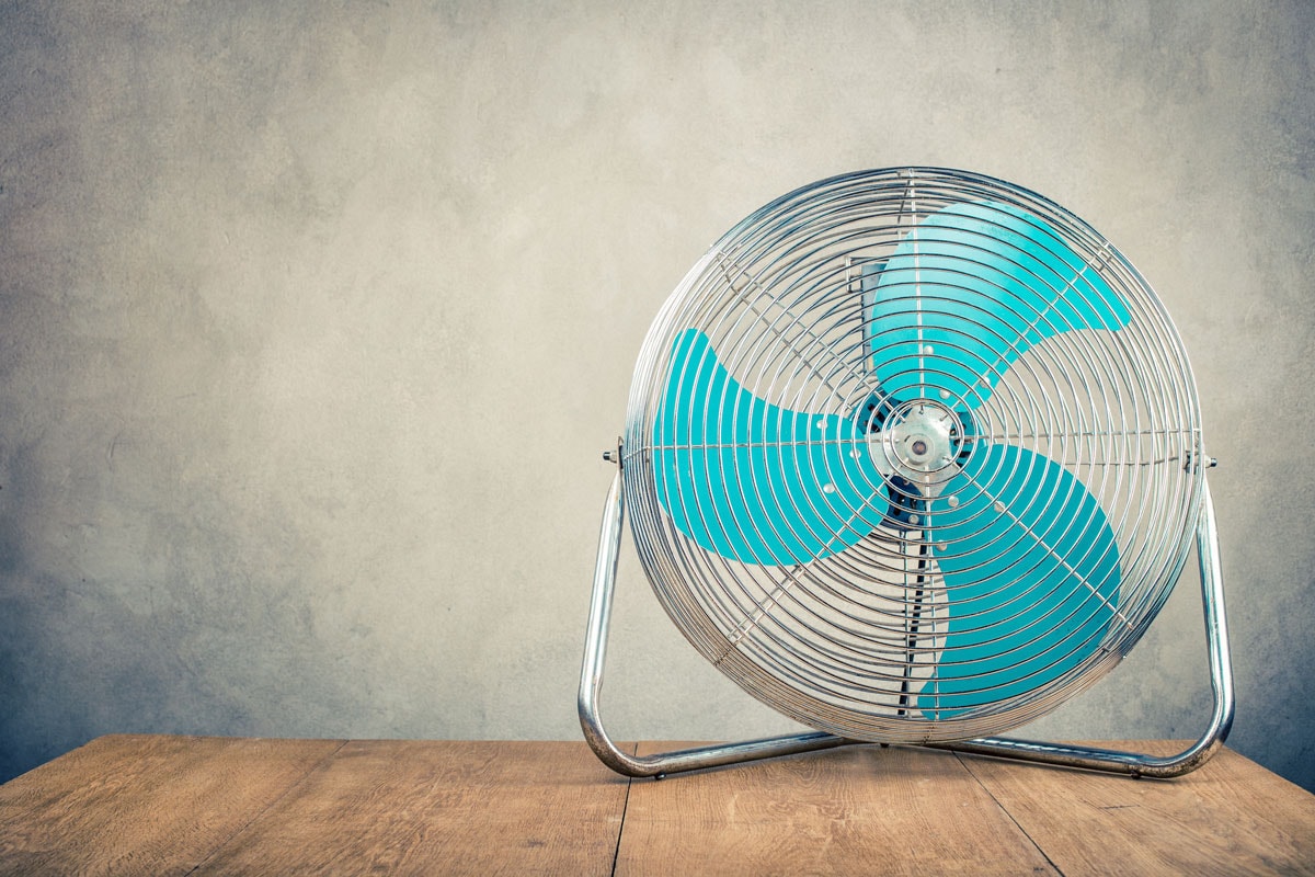 Retro old portable office or home cooling fan standing on desk front concrete wall background.