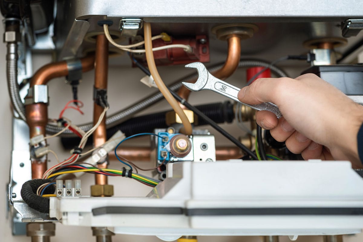 Technician is holding wrench in front of combi gas boiler
