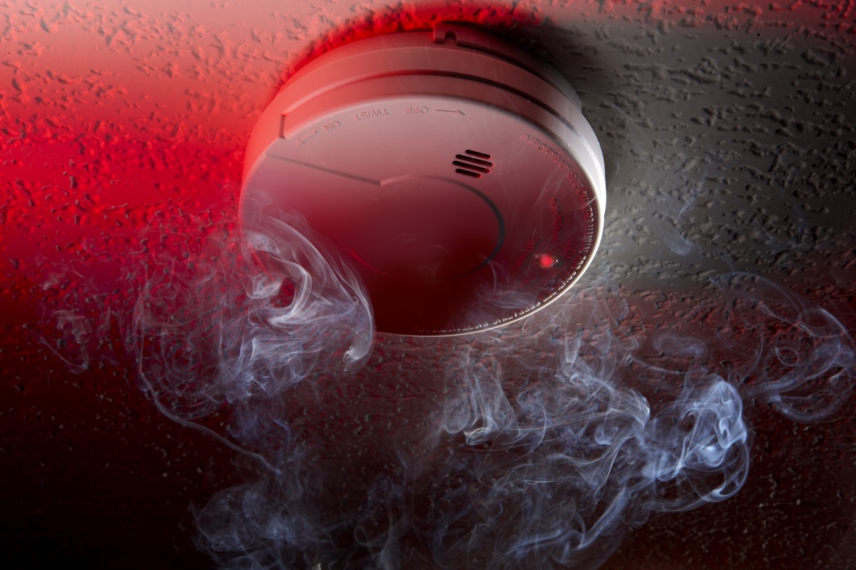 The Alarm Detected Smoke - Close up shot of ceiling mounted smoke detector with white smoke and red warning light