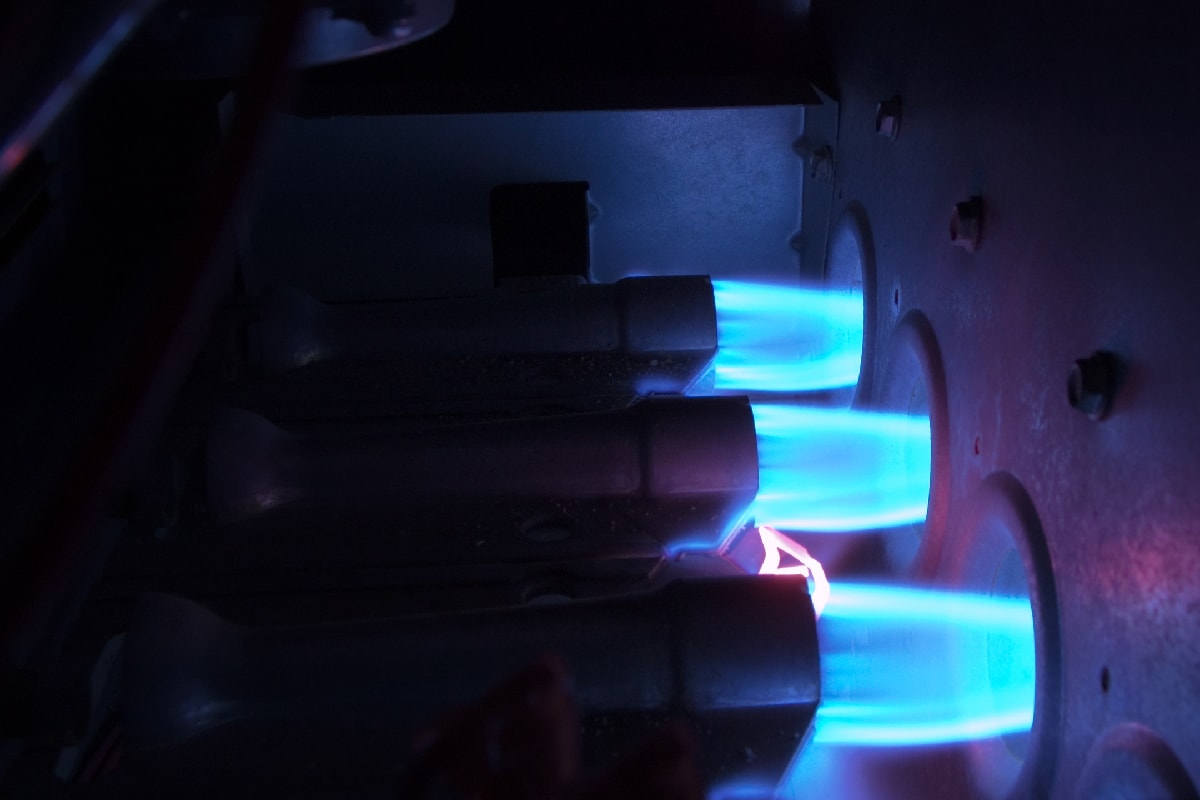 Three natural gas burners with bright blue flames inside an operating gas furnace