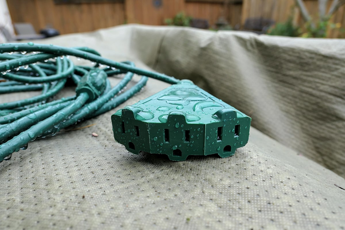 Three prong Green electrical extension cord covered in water from the rain