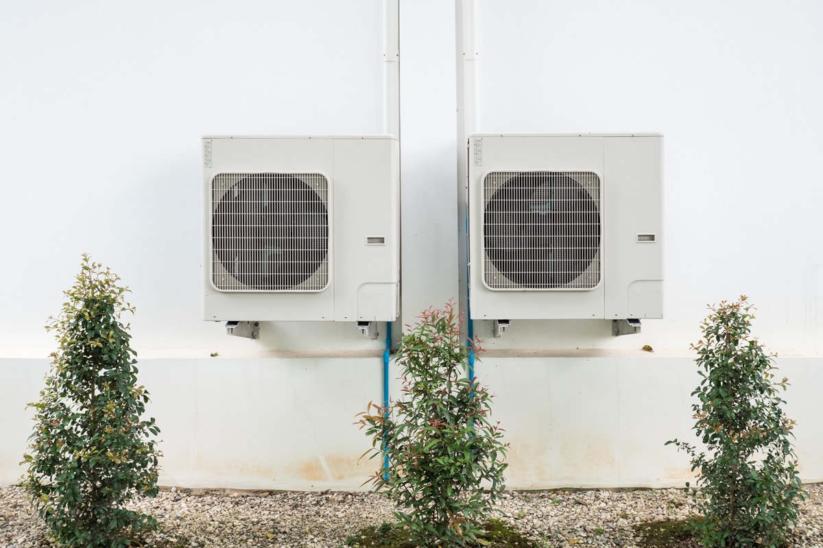 Two air conditioning units hanged on a white concrete wall