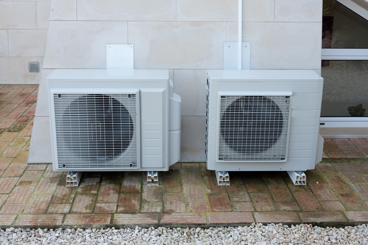 Two air conditioning units mounted on plastic pads outside a house