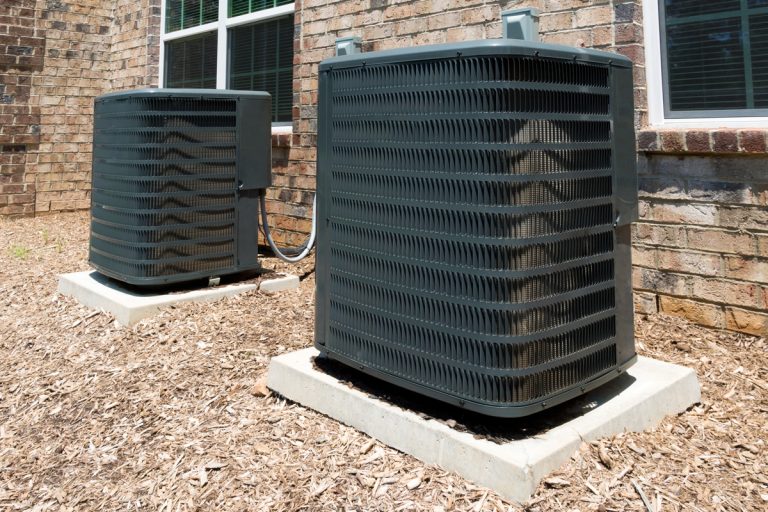 Two huge black air conditioning units mounted on concrete pads, UV Light For HVAC: Pros & Cons [Considerations For Homeowners]