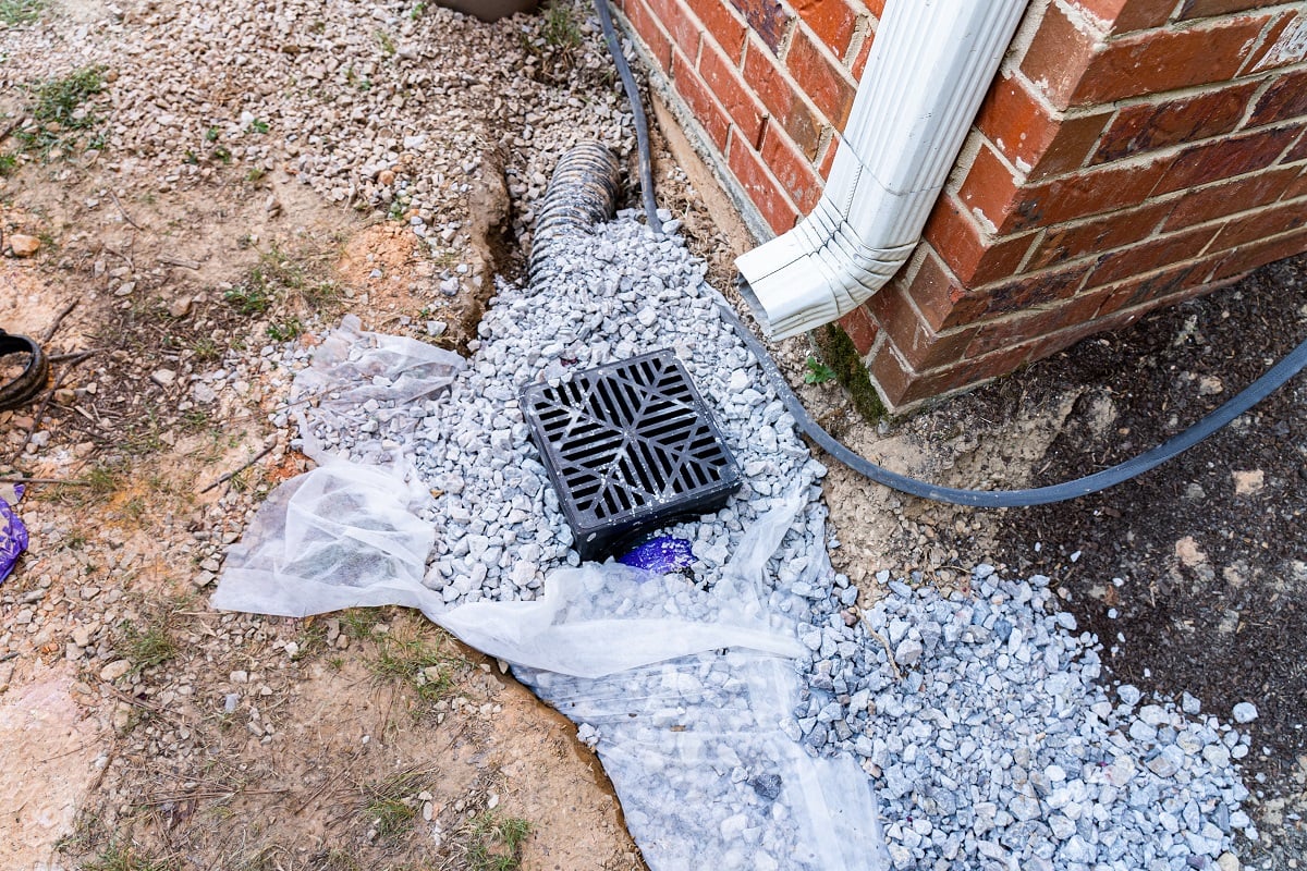 What are the common AC drain line issues - Plastic catch basin installed under a downspout to alleviate drainage issues against a red brick home