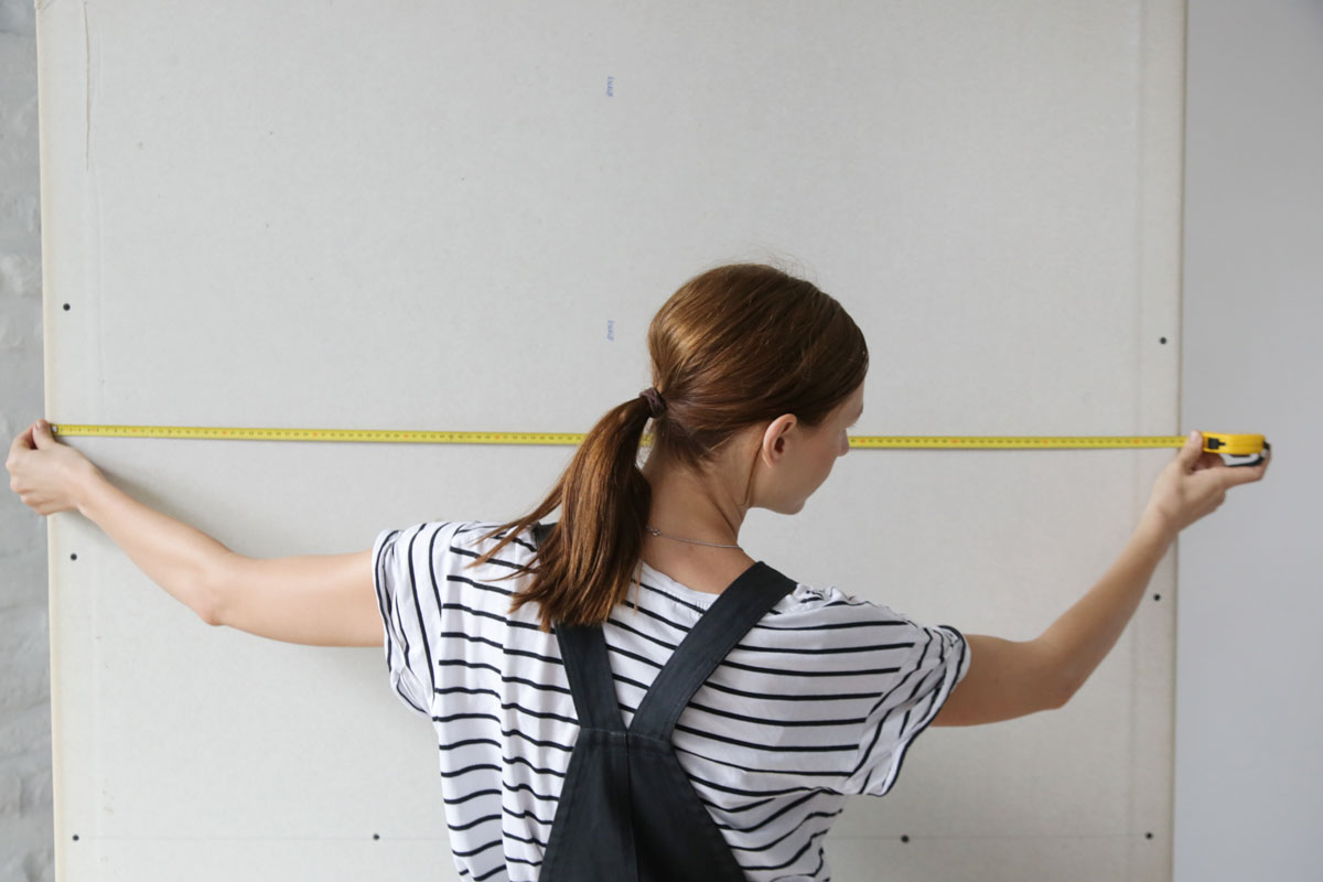Woman-holding-a-meter,-measuring-dimensions-on-plasterboard-panel---DIY-home-improvement