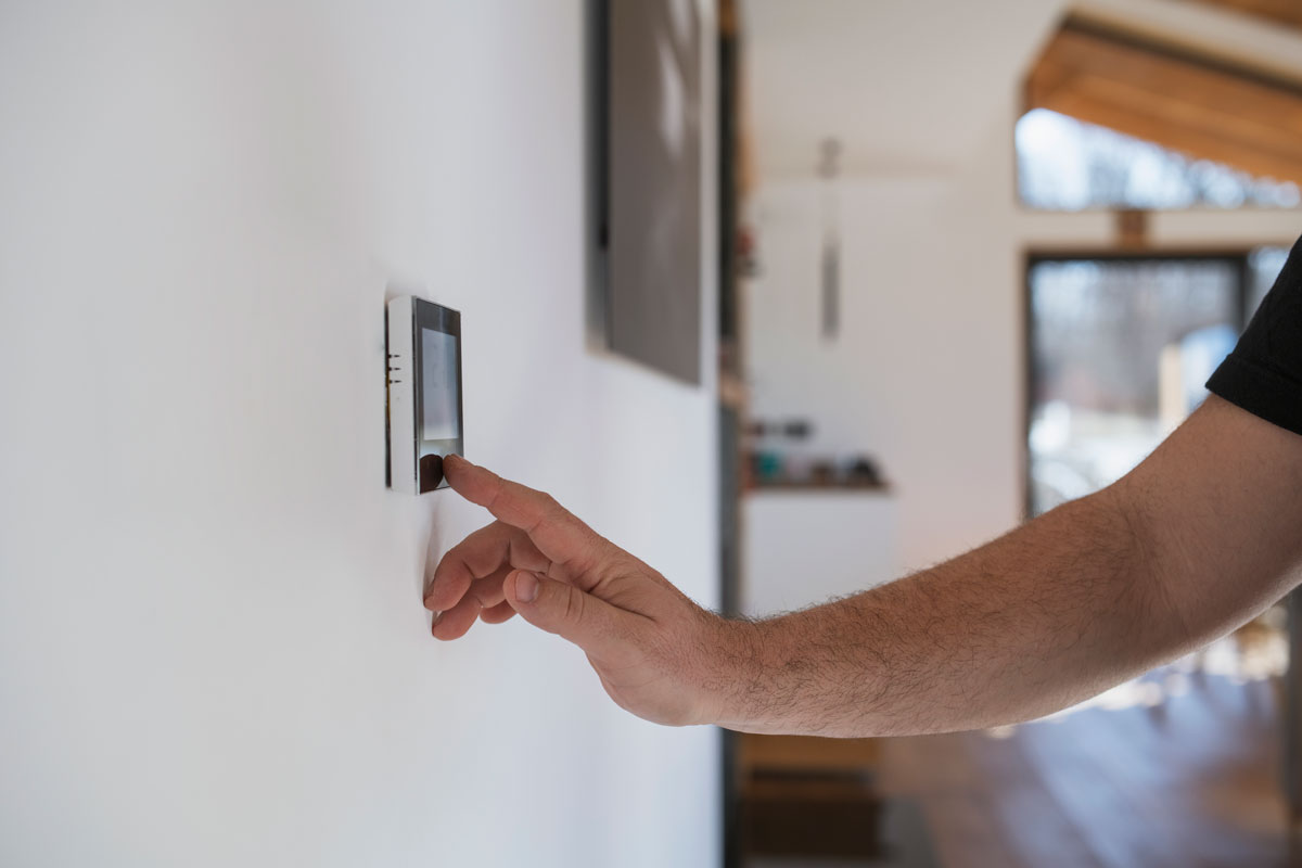 man at home adjusting thermostat with device on the wall