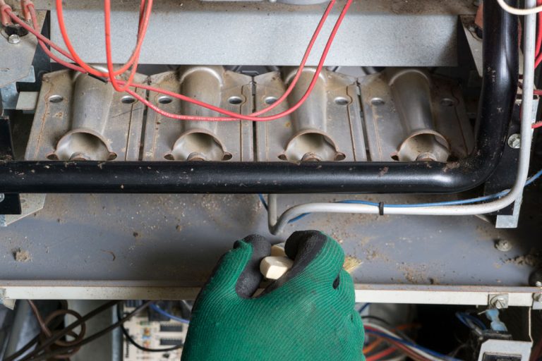 photo of a man hand wearing green gloves cleaning the furnace access panel, How To Remove Access Panel On Carrier Furnace