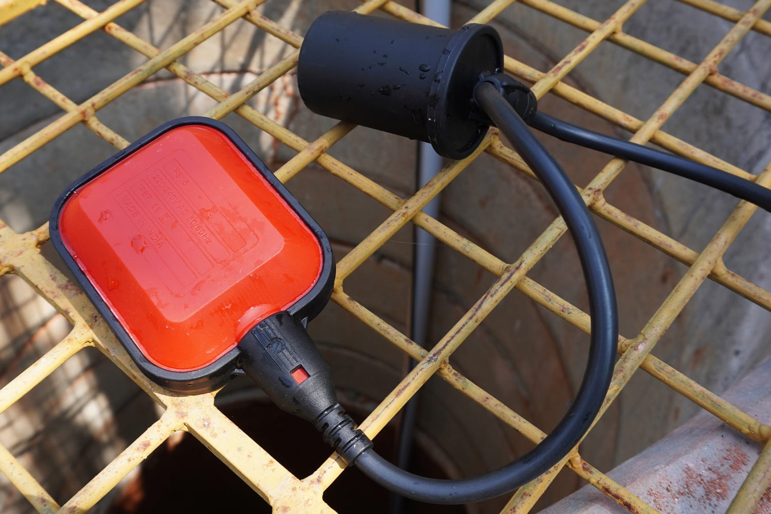 A float switch, a device used to detect the level of water in a tank. Water level sensor kept of the wire mesh over a well, flat lay image.