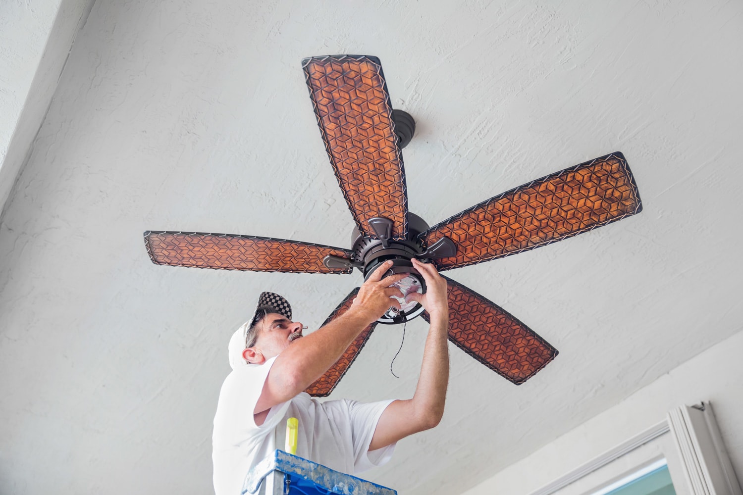 A real electrician stands on a ladder while finishing hanging a ceiling fan