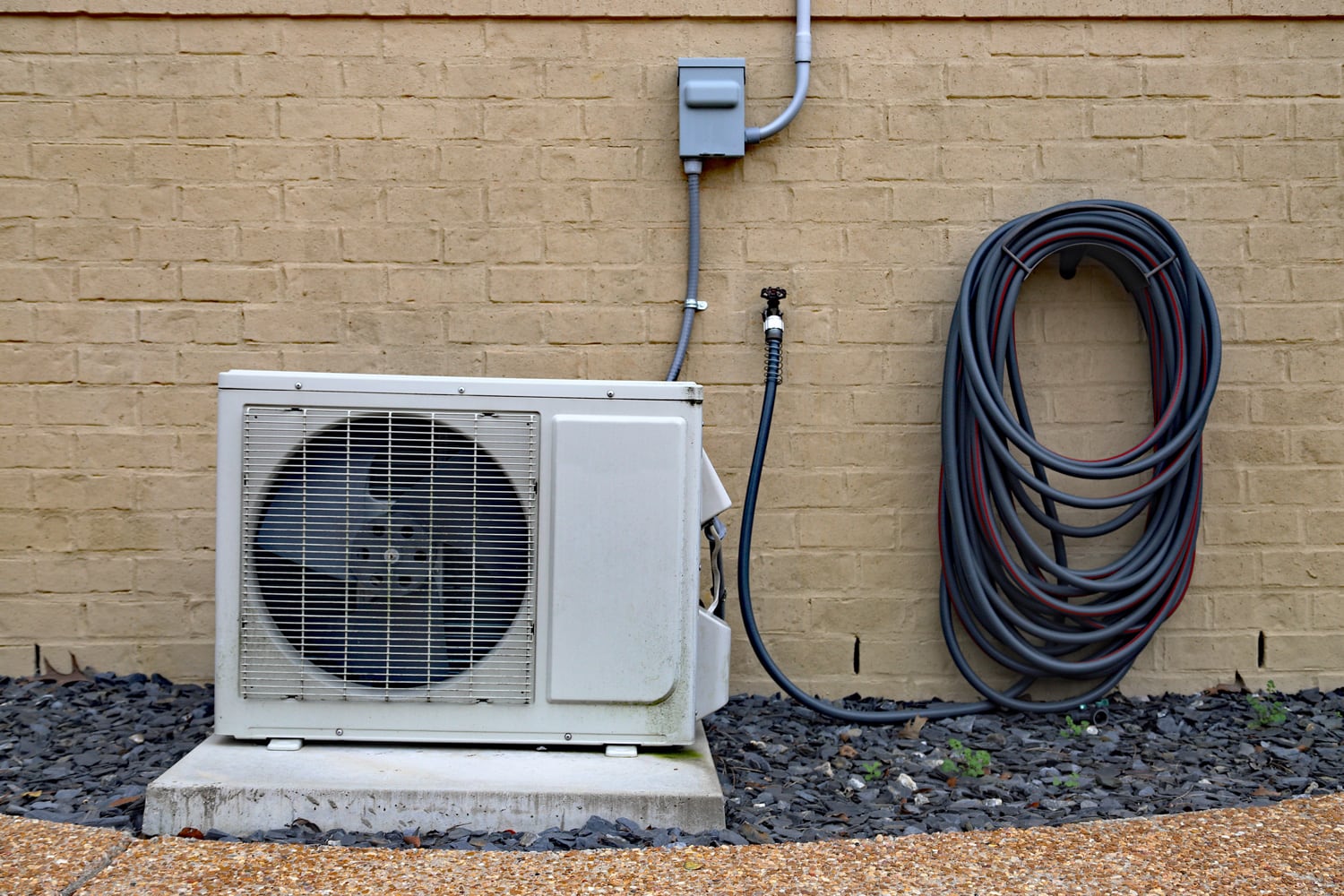 Air Conditioner mini split system next to home with painted brick wall and space for text copy