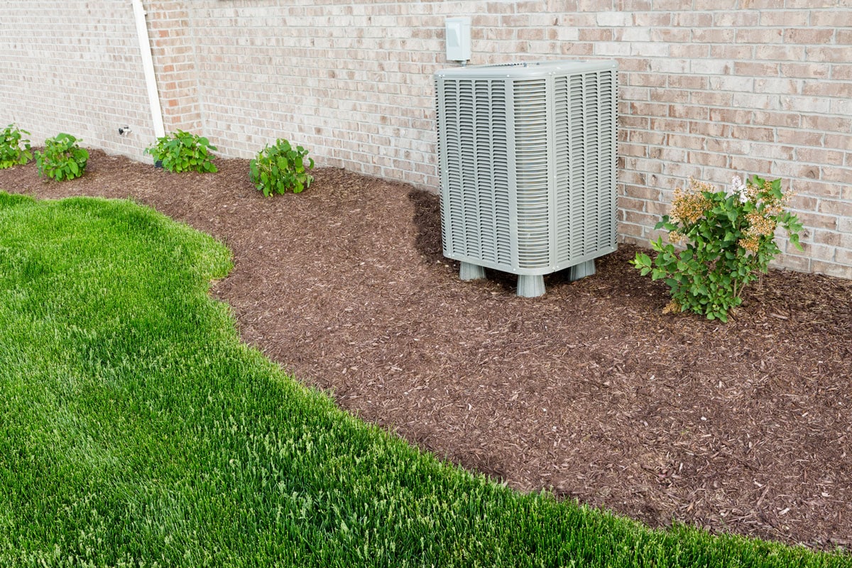 Air conditioner condenser unit standing outdoors in a garden in a neat clean mulched flowerbed for easy access for maintenance