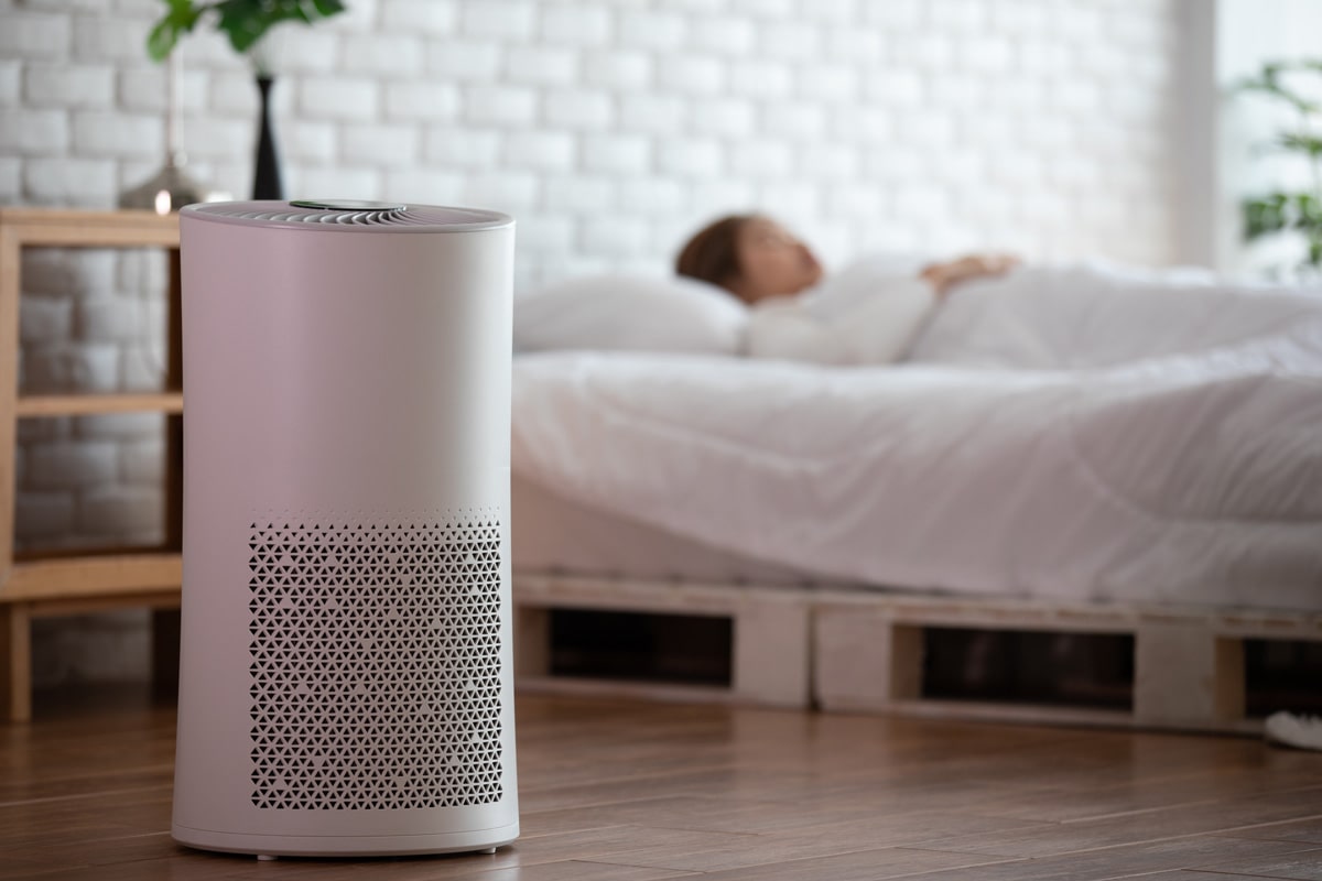 An air purifier inside a bedroom with a woman sleeping on the bed