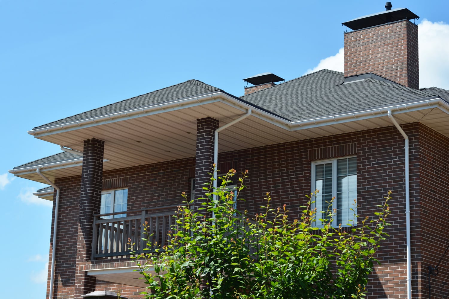 Brick house with asphalt shingles roof, chimney, balcony, rain gutter pipeline and soffit boards. Close up on UPVC Soffit Boards.