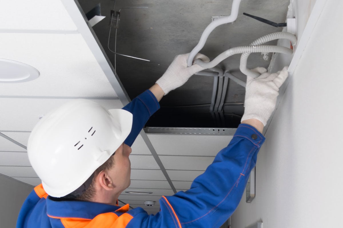 Electrician in a protective helmet, fixes a malfunction in communications hidden in the suspended ceiling