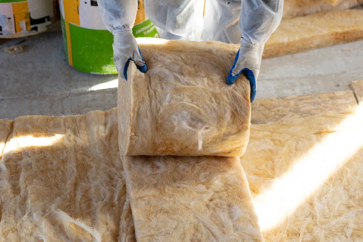 Cropped view of one foreman in overalls working with rockwool insulation material, standing inside new house under construction, holding warmth layer in hands