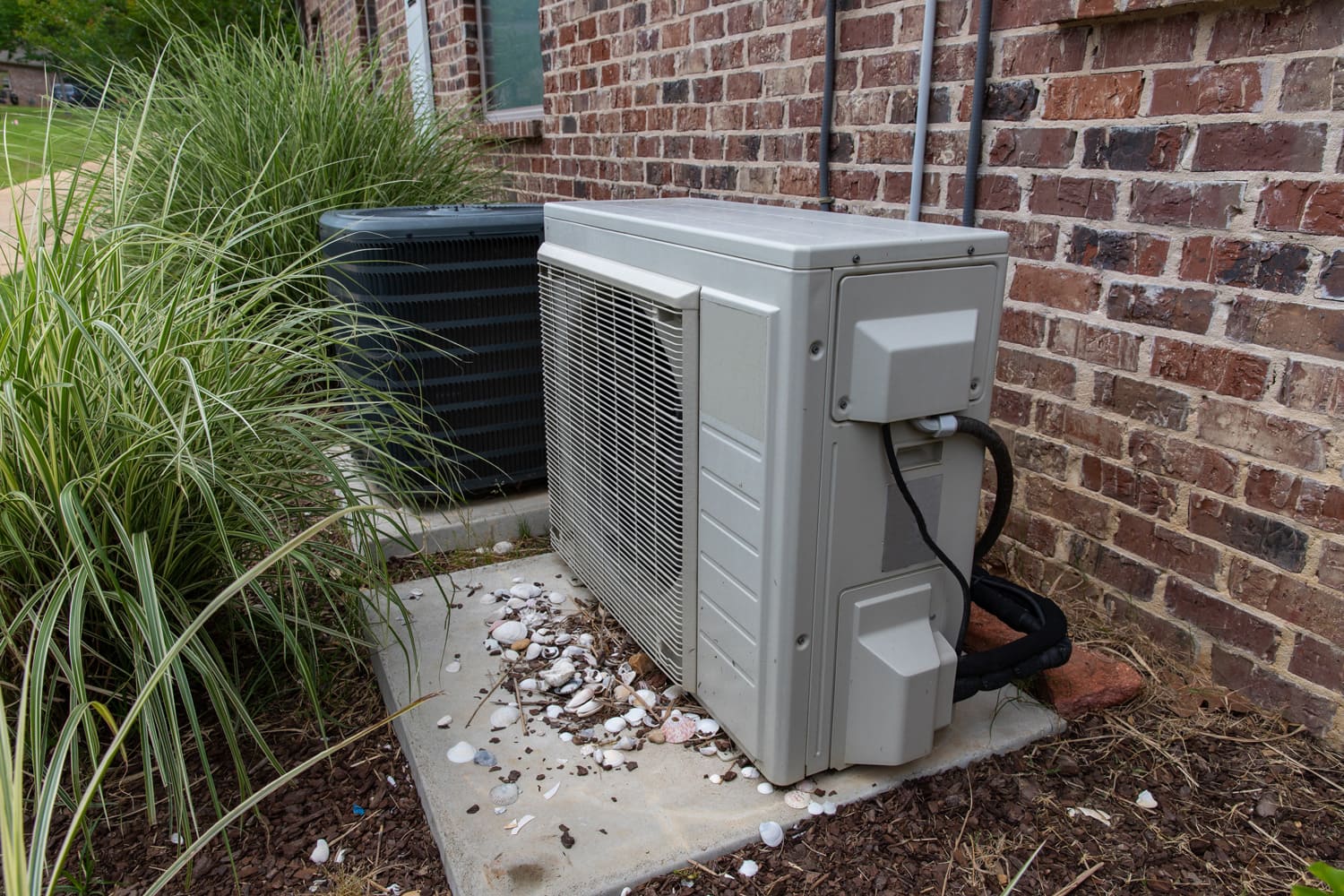 HVAC Air Conditioner Compressor and a Mini-split system together next to each other, next to a brick home.