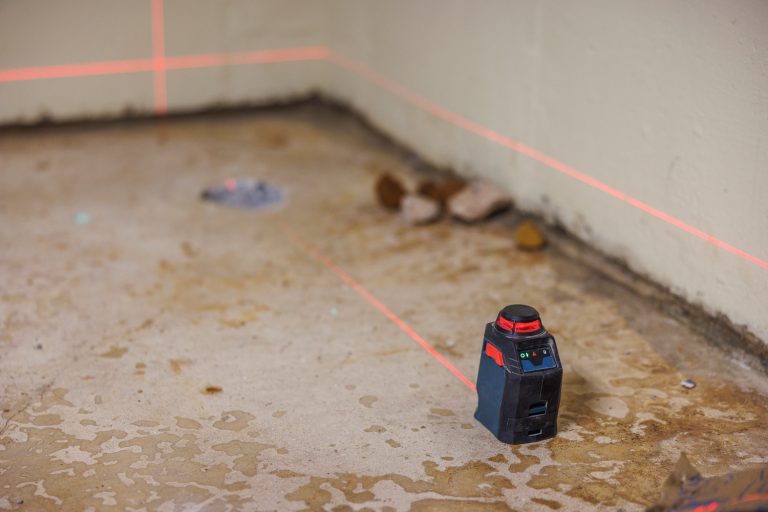 Measurements with a laser ruler in the basement as a part of the radon mitigation system installation. Selective focus on the foreground with defocused background. -What Is A Radon Mitigation System & How Does It Work? [Complete Guide For Homeowners]
