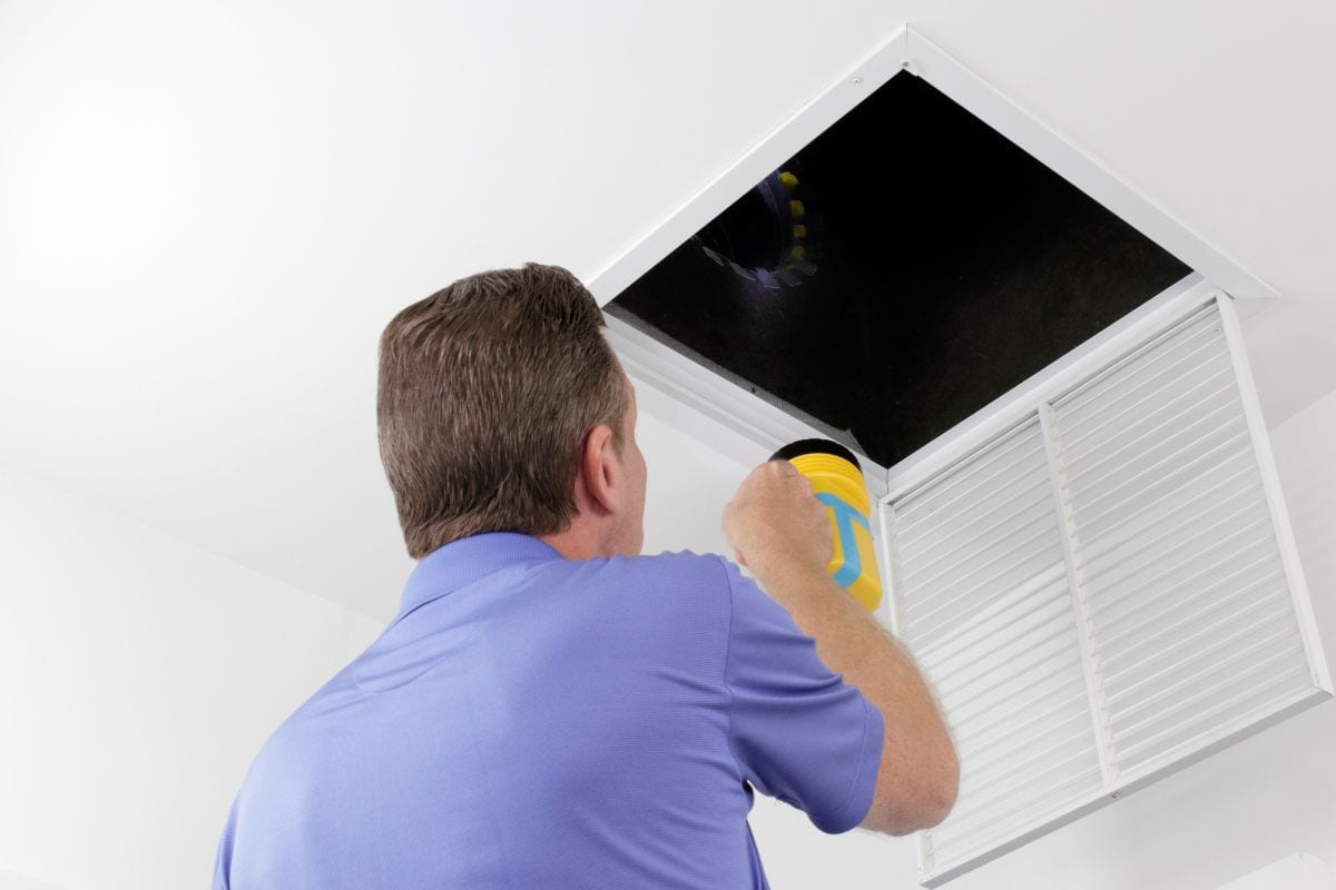 Man Inspecting an air duct with a flashlight