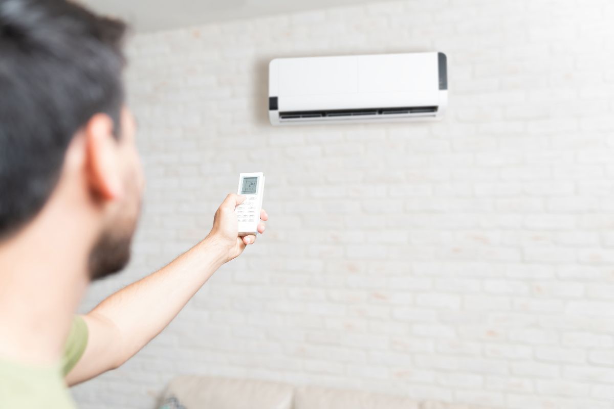 Mid adult man adjusting temperature of air conditioner using remote control at home