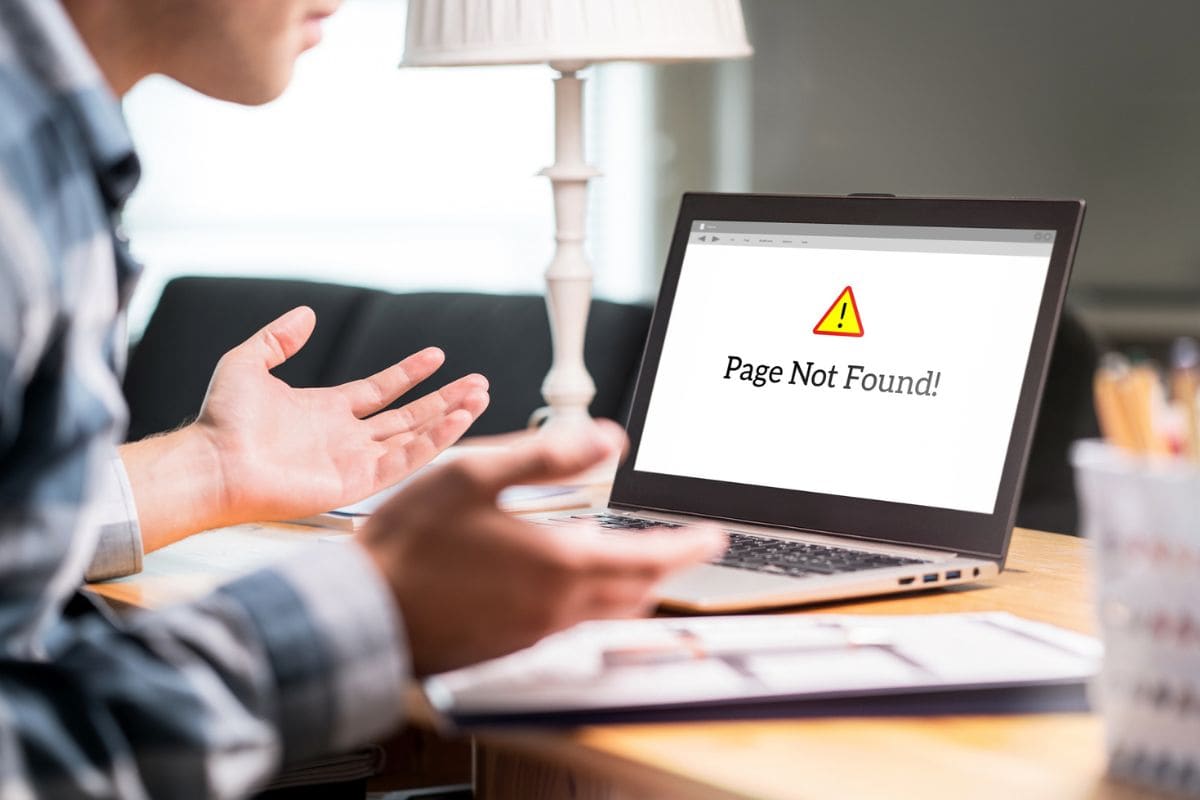 Page not found and error in laptop. Bad or slow internet connection. Frustrated man spreading hands in home office desk. Broken computer not working. Online information problem. Alert icon in website.
