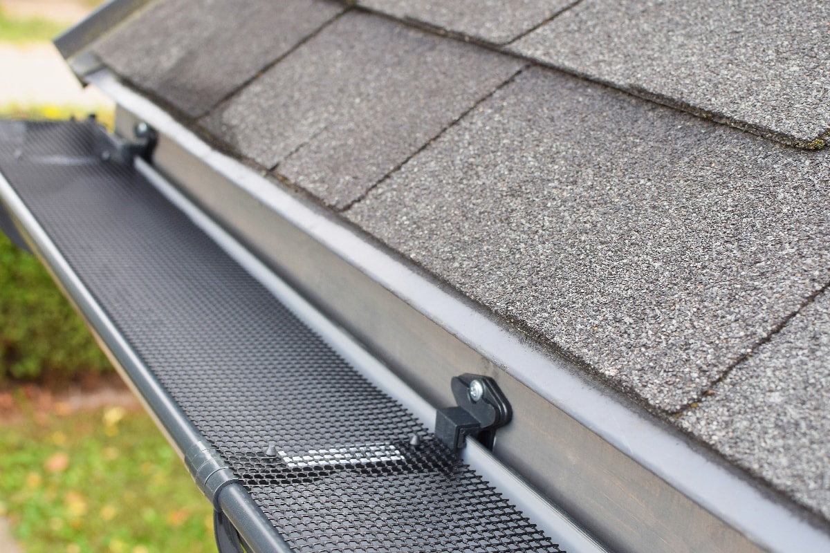 Plastic guard over new dark grey plastic rain gutter on asphalt shingles roof