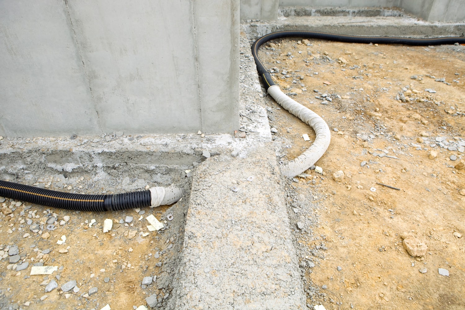 This image shows the initial pipe component of a sub-slab radon mitigation system. This is an active system which will include a fan to depressurize the area below the basement floor. The drain tile (pipe) will be covered with rock, which will be covered with a membrane and then a concrete slab will be poured. The pipe runs through a concrete footing for a supporting wall and the surrounding walls are poured concrete