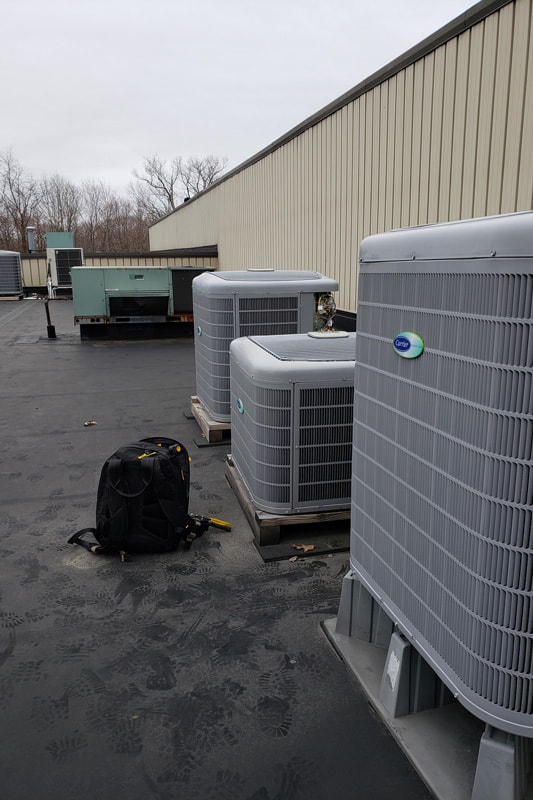 Technicians tools placed in front of multiple Carrier Infinity series HVAC Air conditioning condensing units on a roof top of a commercial building. 