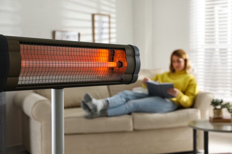 Woman reading book in living room, focus on electric infrared heater - How Do You Reset An Infrared Heater [Step By Step Guide]