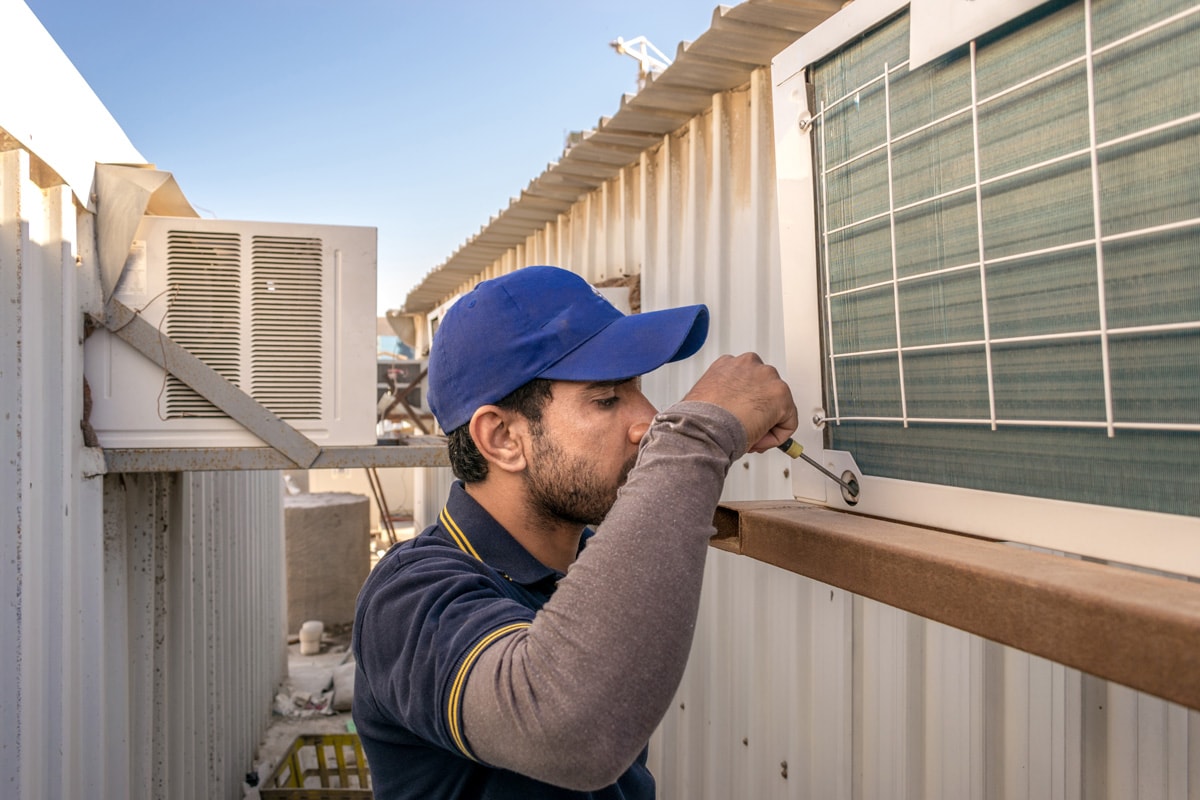 a professional electrician man is fixing the window unit of an air conditioner at the roof top of a building and wearing blue uniform and head cap