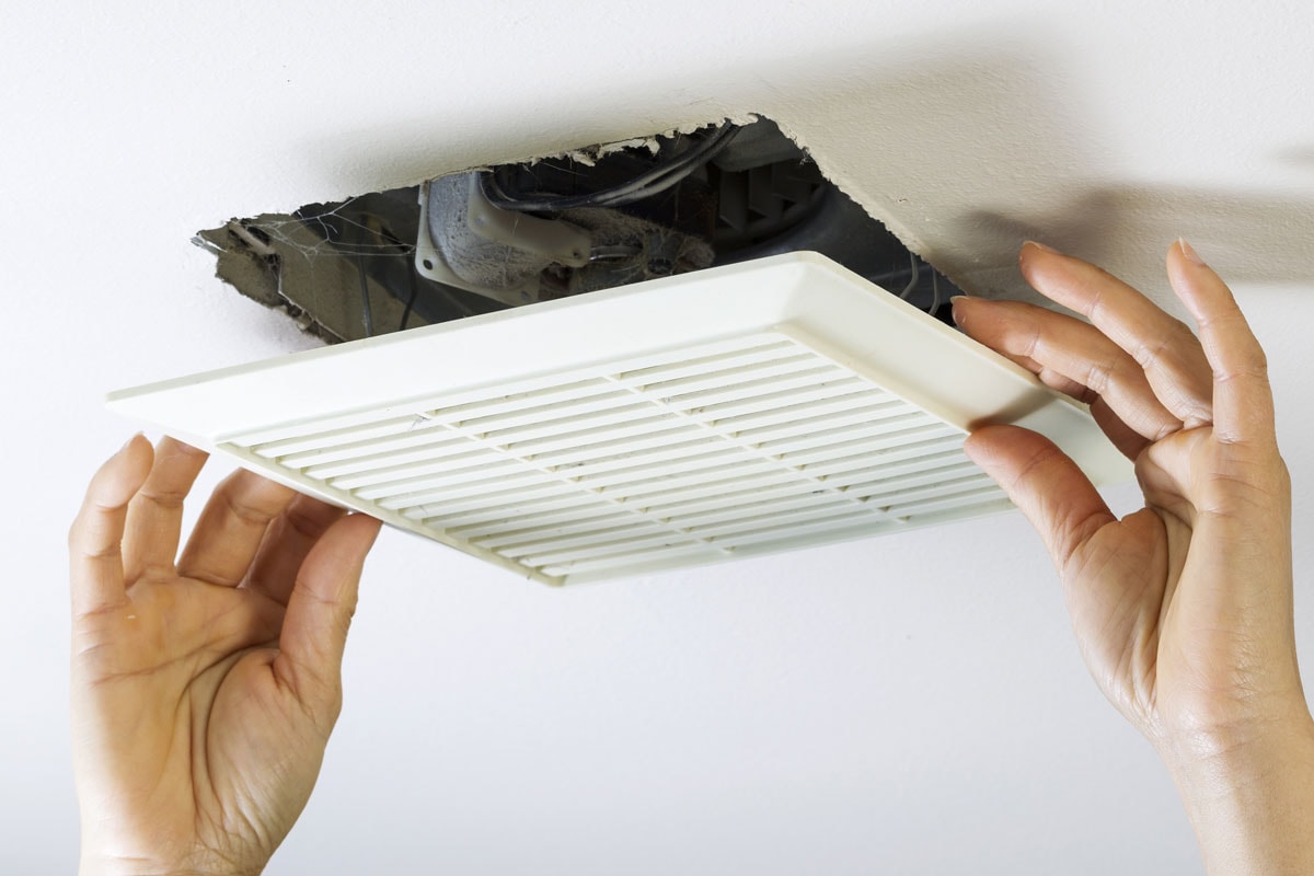 horizontal photo of female hands removing bathroom fan vent cover from ceiling