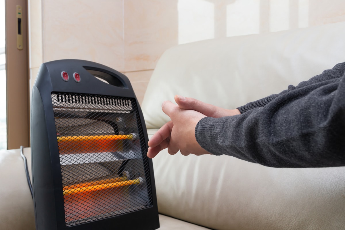 man sitting on sofa with an electric heater near his hands