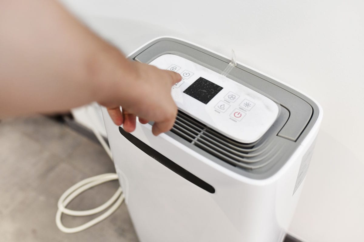man's hand turning on a dehumidifier in the entrance of a house or office
