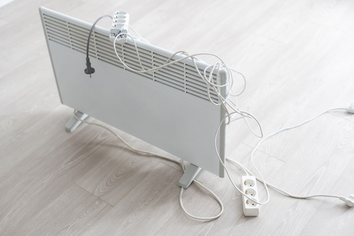 A white electric heater in a floor with an extension chord