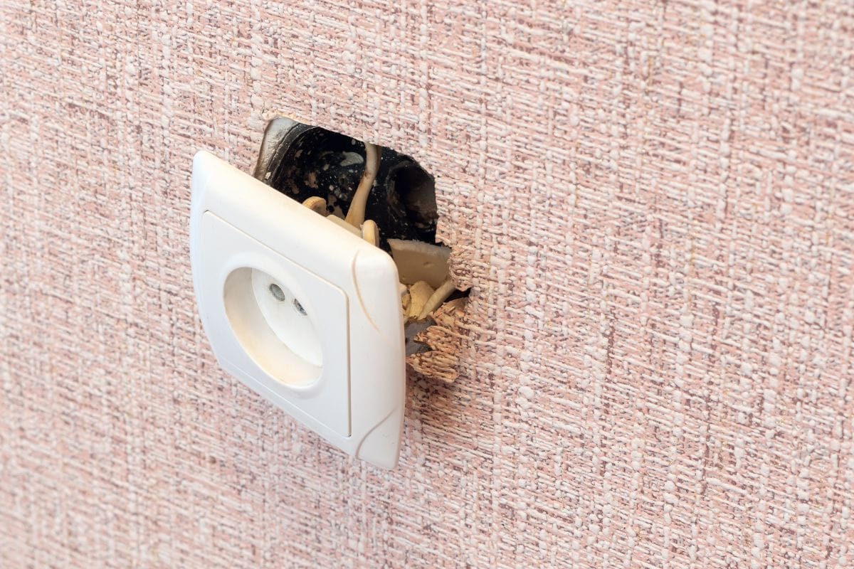 An old broken electrical outlet fell out of the wall, danger of electric shock.