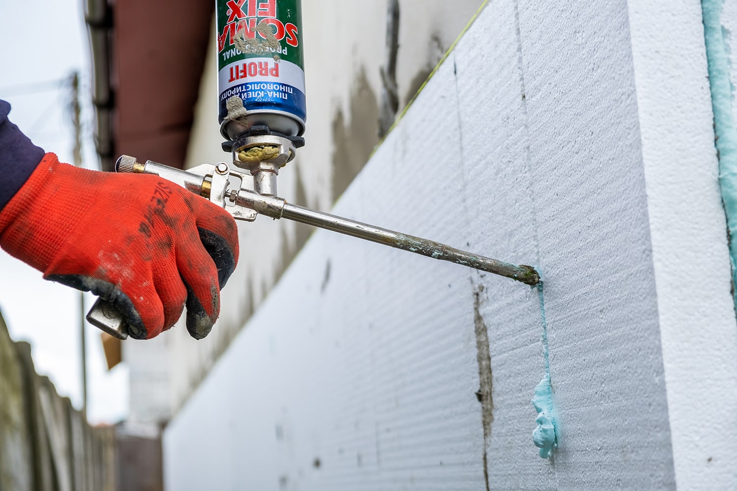 Construction worker installing styrofoam insulation sheets and filling space between with expanding foam on house facade wall for thermal protection