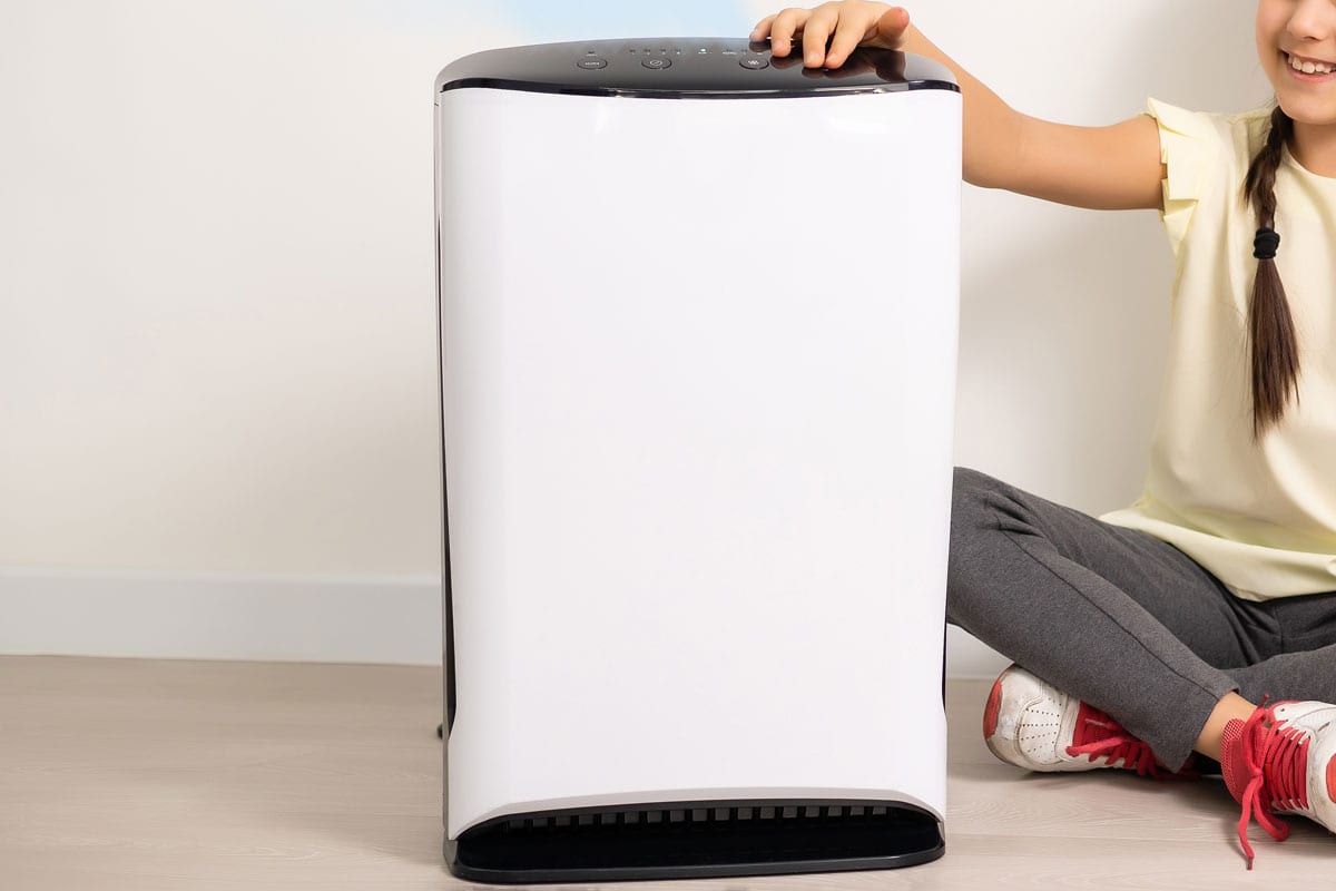 Cute little girl standing breathing at air purifier