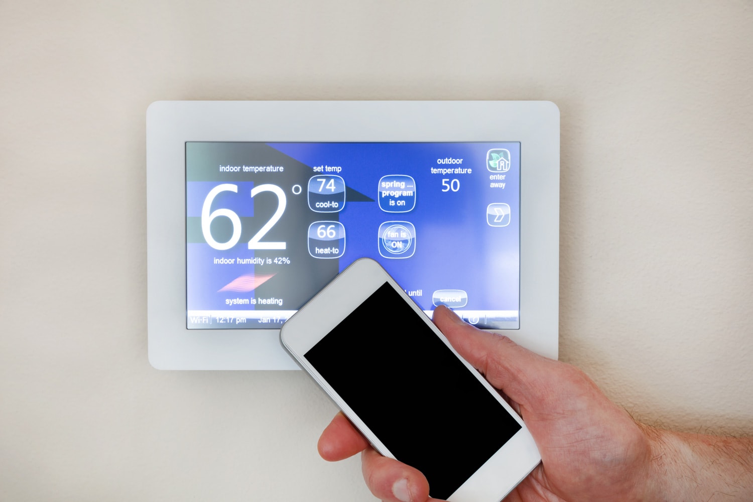 Male hand holding smart phone to operate heating or cooling of thermostat for home 