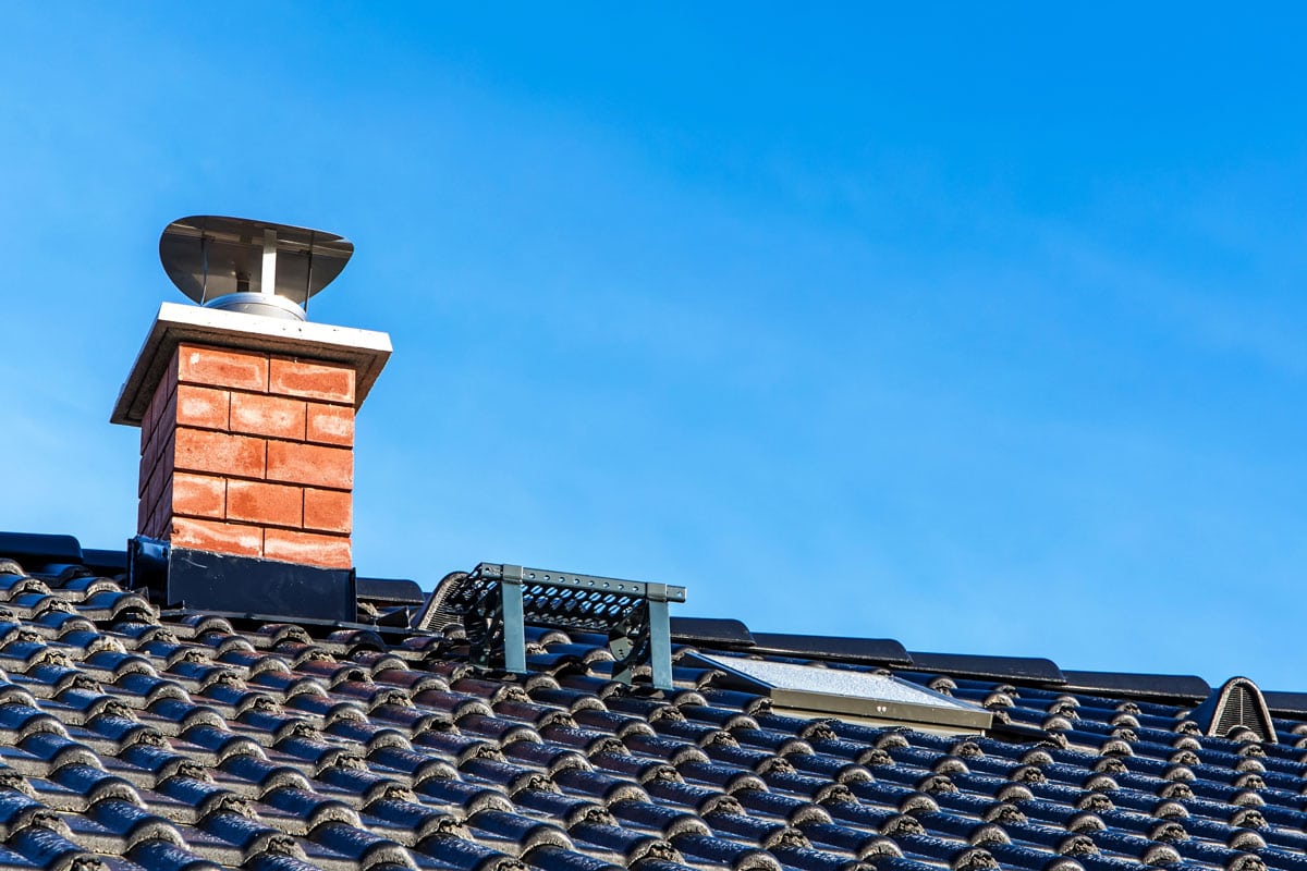 New black tiled roof with chimney. New roof of a detached house with chimney against the sky