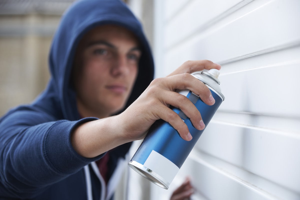 Teenage Boy Spray Painting Garage Door 