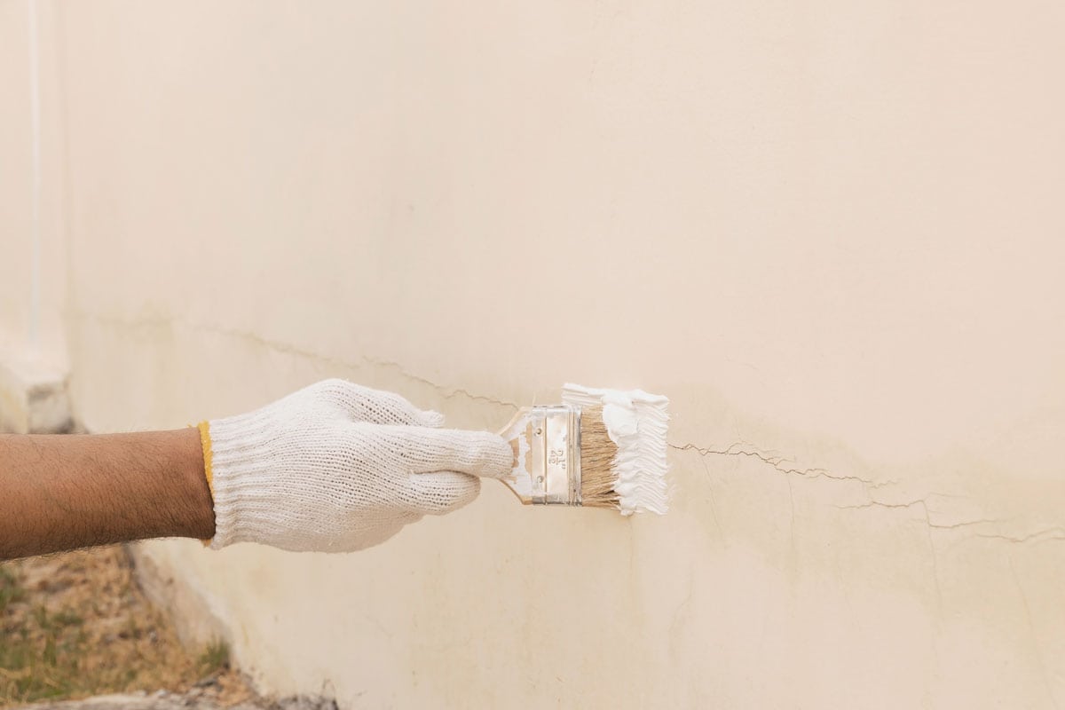a hand with white cloth gloves that is being used to transform paint to seal the cracks on the concrete wall