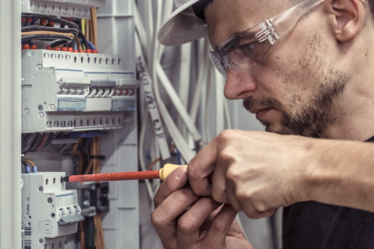 a male electrician works in a switchboard with an electrical connecting cable
