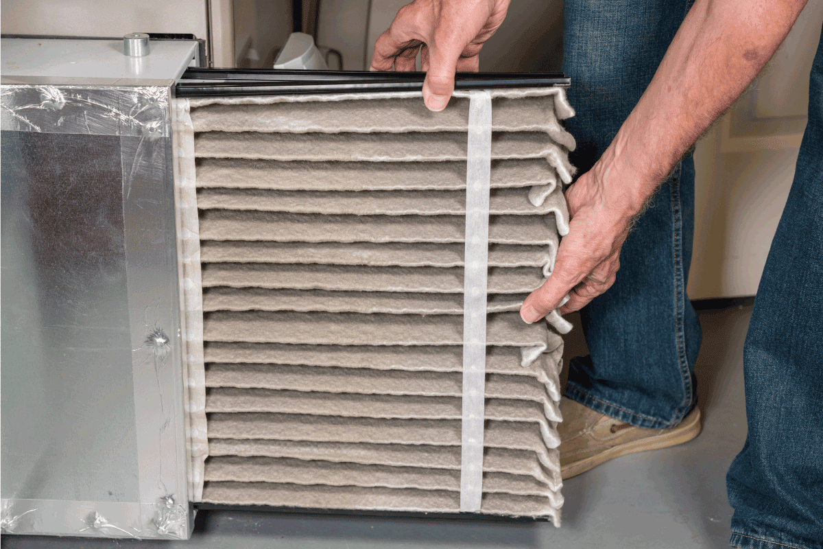 man changing a folded dirty air filter in the HVAC furnace system in basement of home