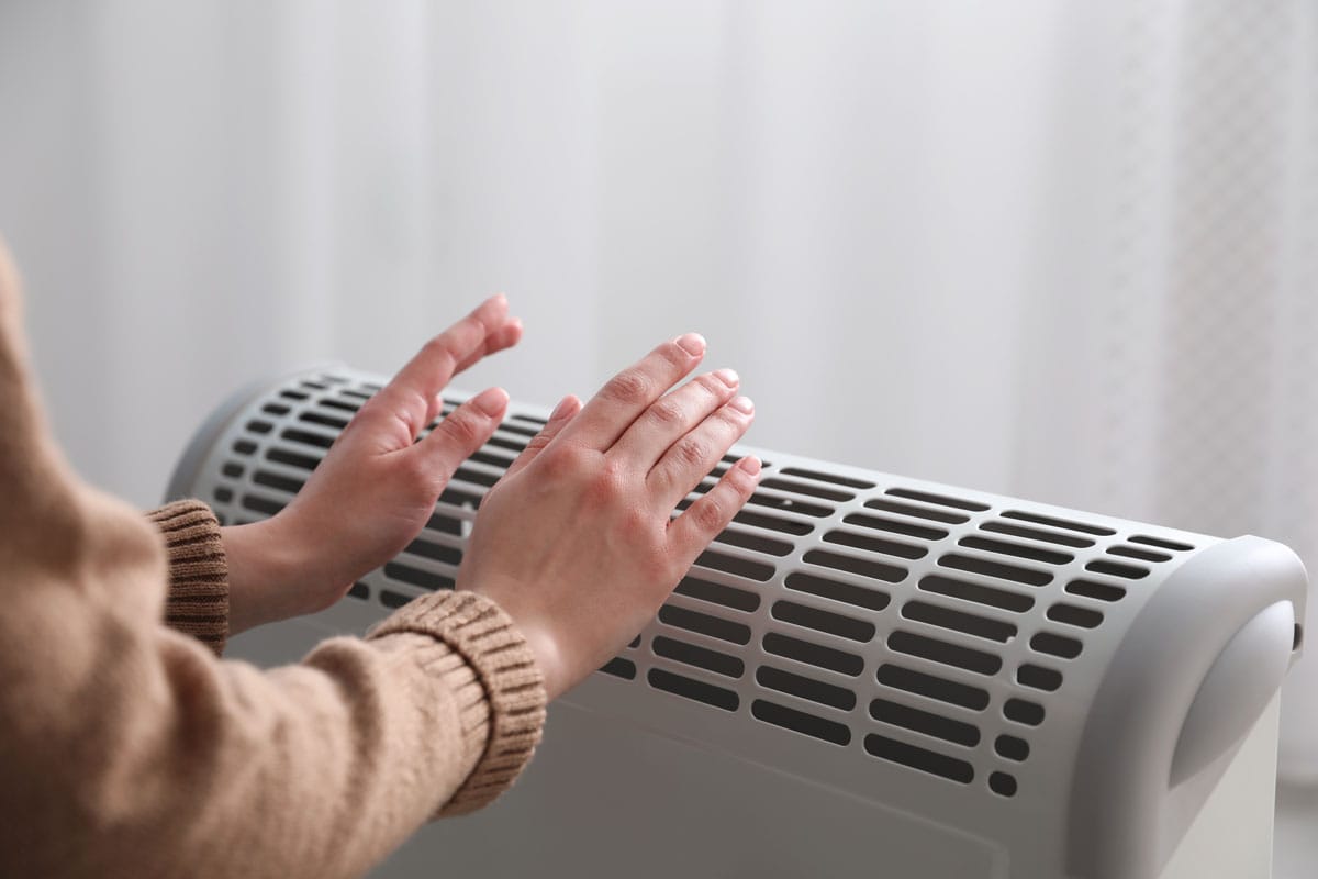 woman warming hands near electric heater