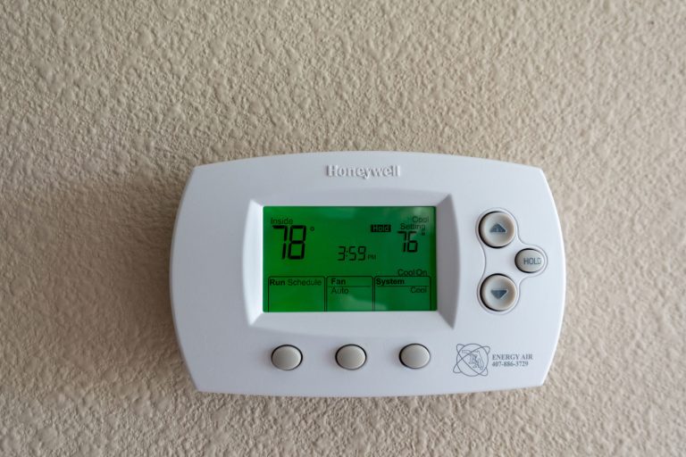 A Honeywell programmable thermostat to control the air conditioner and heater in a home. Copy space is above Thermostat, How To Control A Honeywell Thermostat From Your Phone [Step By Step Guide]