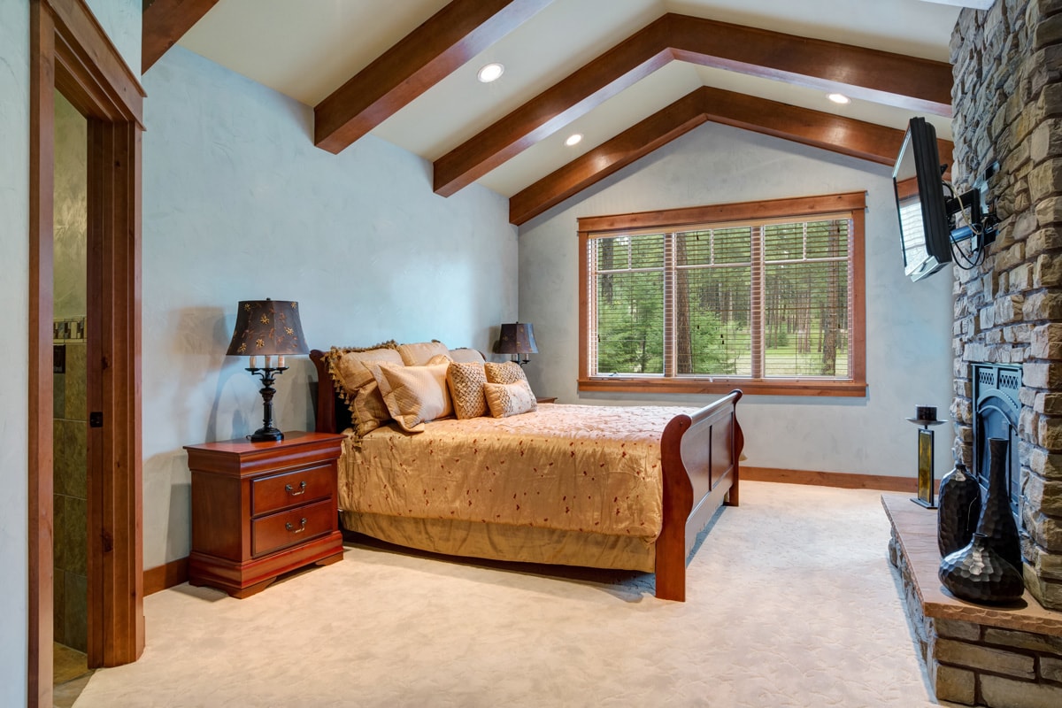vaulted ceiling with wooden beams over the wood sleigh bed facing stone wall fireplace. Northwest, USA