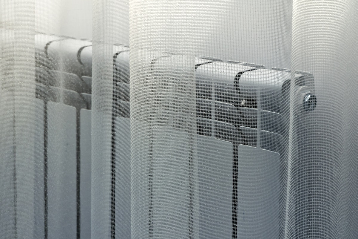 Heating radiator in the room behind a light white curtain