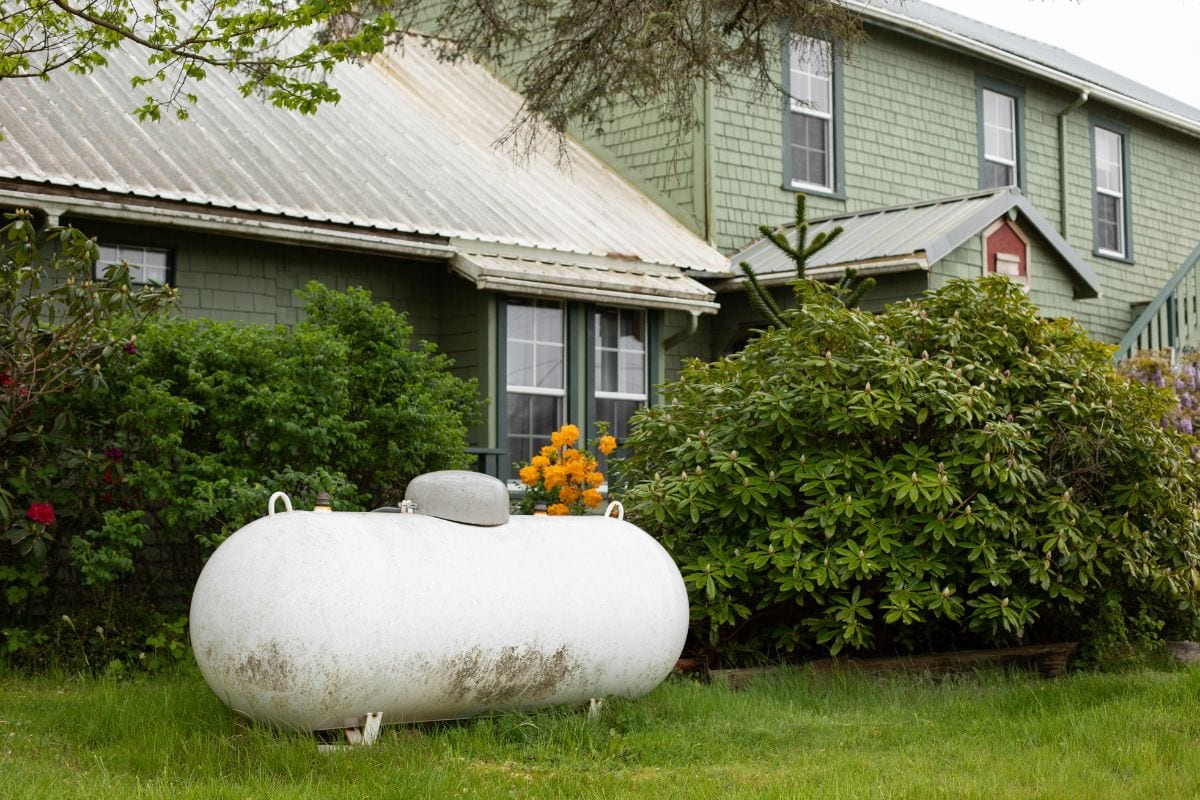 Large propane tank in the yard of a rural home, with a house in the background and space for text on the right