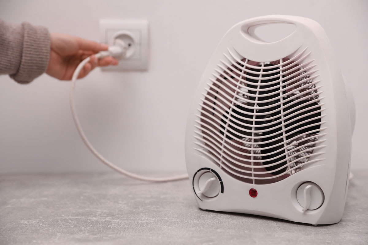 Woman plug in modern electric fan heater indoors, focus on device